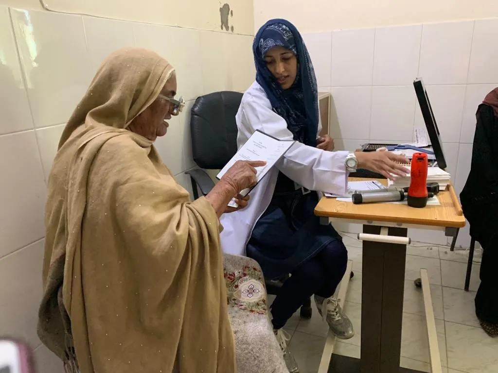 A doctor at a camp writes a prescription while a patient waits